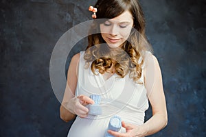 Expectant mom with baby boy booties standing over dark backdrop. Pregnancy, maternity concept.