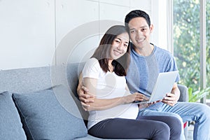 An expectant mother and father are sitting in the living room with a laptop computer