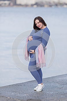 Expectant mother in sportswear posing with hands on stomach against sea