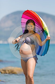 Expectant mother in striped swimwear under rainbow umbrella