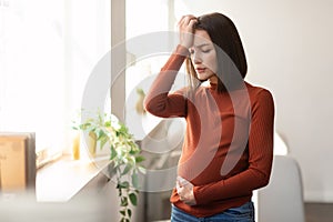 Expectant woman at home feeling unwell suffering with headache