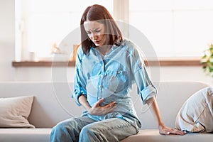 Expectant woman touches her belly in discomfort and pain indoors