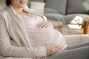 Smiling young female future mom holding hands on pregnant belly