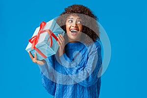 Expectations, holidays and winter concept. Excited cheerful african-american woman shaking box with gift, want unwrap