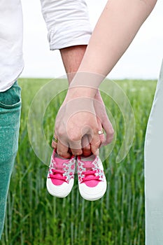 Expecting a baby. A woman and a man hold baby`s shoes in  nature