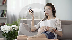Expecting lady listening to relaxing music on cellphone and rubbing belly