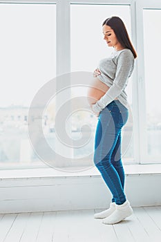 Expecting woman holding her baby bump standing in living room