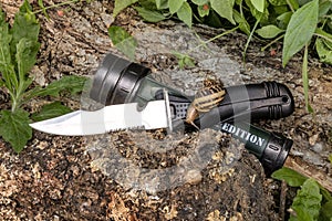 Expedition knife and flashlight waterproof on the tree trunk in the forest