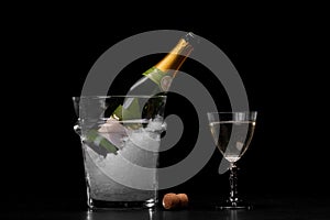 An expensive bottle of champagne in a transparent bucket filled with ice on a black background. Celebration concept.