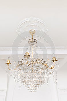 Expensive interior. Large electric chandelier made of transparent glass beads. White ceiling decorated with stucco