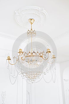 Expensive interior. Large electric chandelier made of transparent glass beads. White ceiling decorated with stucco