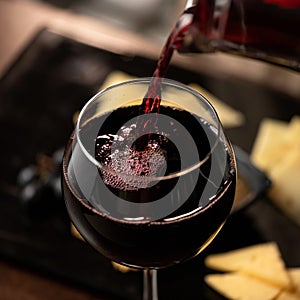 Expensive Red wine pouring into wine glass. Wineglass with merlot or sauvignon on Blurred background. Close up shot