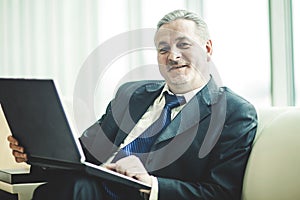 Experienced businessman working on laptop sitting on sofa in a private office