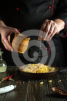 An experienced chef salts pasta with vegetables in a plate on the kitchen table. The concept of preparing a delicious breakfast at