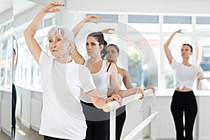 Experienced choreographer teaches ballet dancers movements at ballet barre in choreographic studio