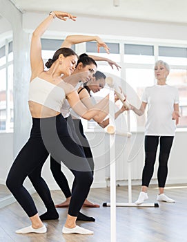 Experienced choreographer teaches ballet dancers movements at ballet barre in choreographic studio