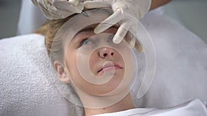 Experienced cosmetologist marking position of wrinkles on girls forehead
