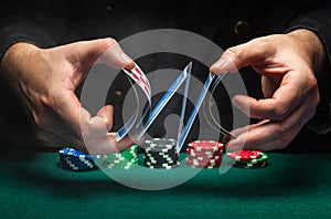 An experienced dealer or croupier shuffles playing cards in a club over a green table with playing chips. The concept of playing