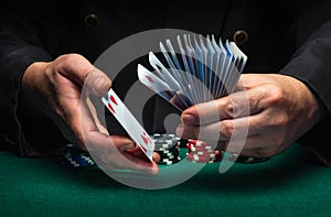 An experienced dealer or croupier shuffles playing cards in a club over a green table with playing chips. The concept of playing