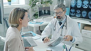 Experienced doctor discussing MRI scan with female patient talking in hospital room