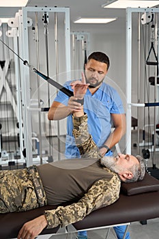 Experienced doctor helps patient perform exercises to stretch arm muscles