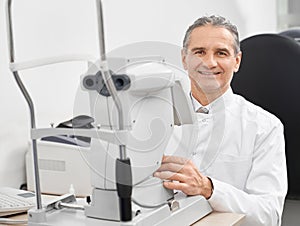 Experienced doctor ophthalmologist posing with slit lamp.