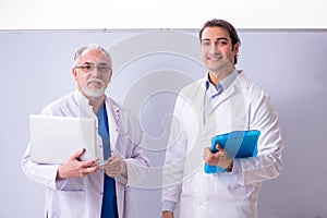 Experienced doctor teaching young male assistant using computer