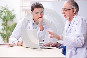 Experienced doctor teaching young male assistant using computer