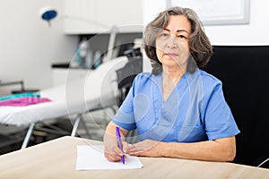 Experienced doctor writes important notes while sitting at workdesk in the cabinet