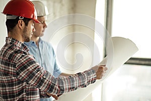 Experienced engineer in red protective hat is teaching the a new worker