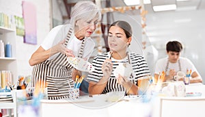 Experienced female ceramicist teaching young girl to paint ceramics in pottery studio photo