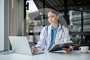 An experienced female doctor is working at her desk in the hospital, reading medical reports online