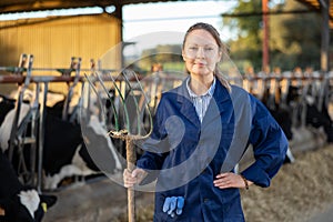 Experienced female farmer standing with pitchfork in livestock farm