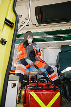 Experienced female paramedic in face mask checks equipment bag