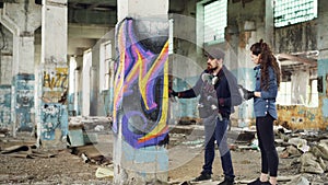 Experienced graffiti artist is teaching his friend to create beautiful images with spray paint, they are standing