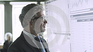 Experienced grey-haired CEO checking data on big screen