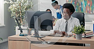 An experienced handsome company employee dressed in a shirt and tie prepares documents on the computer, drafts an