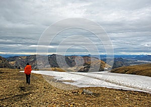 Experienced male hiker hiking alone into the wild admiring volcanic landscape with colorful mountains and snow with big, heavy