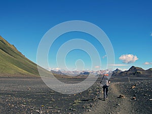 Experienced male hiker hiking alone into the wild with heavy backpack in black desert, Laugavegur hiking trail, Iceland