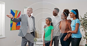 Experienced mature real estate agent shows family around apartment for sale rent points out rooms