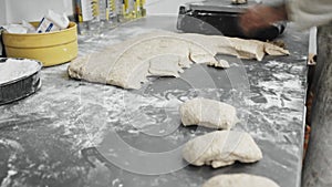 Experienced middle aged woman working with male assistant in bakery, weighing dough and preparing portioned pieces for