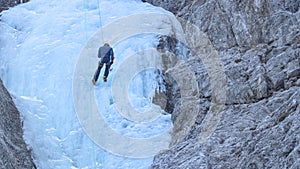 Experienced mountaineer descends down the frozen waterfall after climbing it.