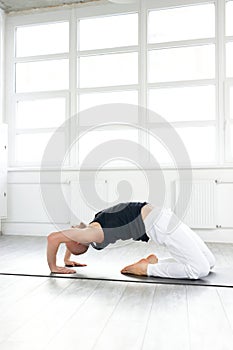 Experienced muscular yogi man working out, bending in Little Thunderbolt Pose or Laghu Vajrasana in studio