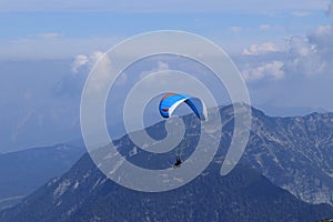Experienced parachutist flies in the right wind and drives a parachute around the Austrian Alps. Paratrooper with a white-blue