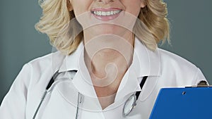 Experienced physician with stethoscope holding folder and smiling into camera