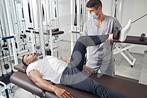 Experienced physiotherapist applying gym equipment for patient leg rehabilitation