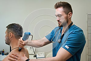 Experienced physiotherapist performing ESWT procedure on adult man