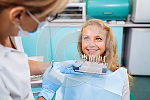 Experienced, professional woman dentist trying on a palette with a set of colors for dental crowns. The whitening procedure