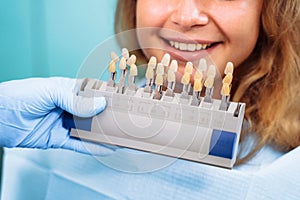 Experienced, professional woman dentist trying on a palette with a set of colors for dental crowns. The whitening procedure