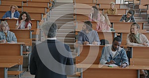 Experienced professor talking to group of students answering questions in classroom